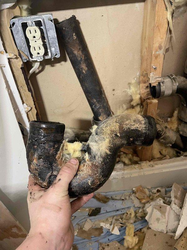 Returned to property to service laundry drain line. Accessed wall cavity to inspect plumbing, identifying a severely deteriorated P-trap with significant black mold/corrosion buildup. Removed damaged P-trap assembly and replaced with new components to restore proper drainage function.
