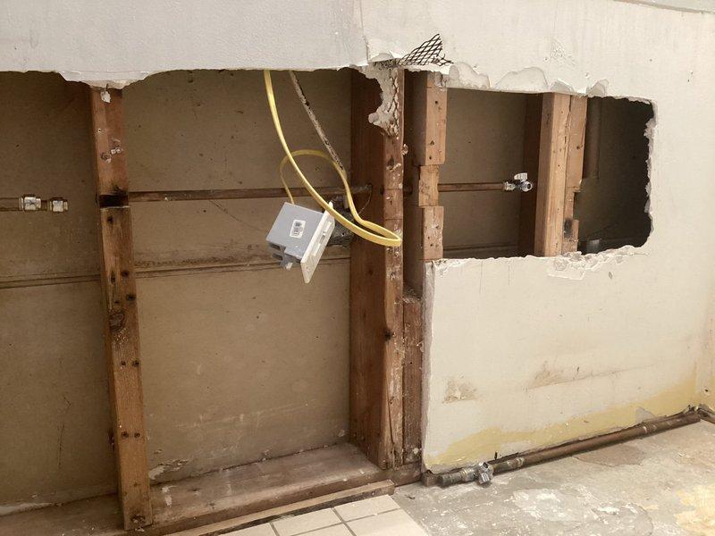 Performed inspection of wall area with exposed pipe system. Found existing capped pipes in opened wall section requiring connection to sink fixture. Identified horizontal drain lines and vertical supply pipes with some water damage around connections. Noted potential connection to boiler system that will need to be addressed during final installation.