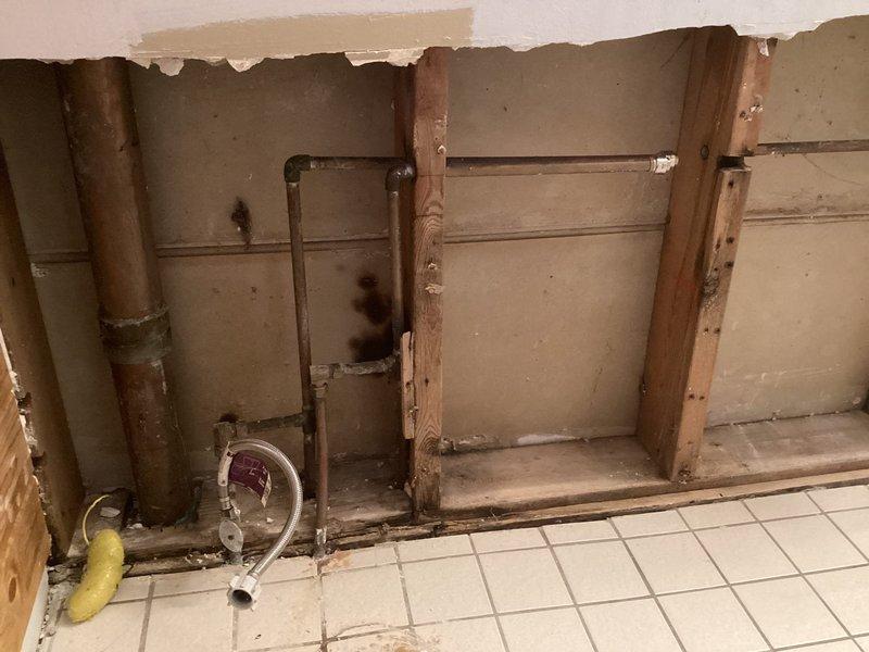 Performed inspection of wall area with exposed pipe system. Found existing capped pipes in opened wall section requiring connection to sink fixture. Identified horizontal drain lines and vertical supply pipes with some water damage around connections. Noted potential connection to boiler system that will need to be addressed during final installation.