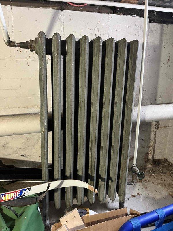 Conducted site assessment for boiler replacement lead from Sam K. Inspected existing heating system, which includes aged cast iron radiators showing signs of wear. Took detailed measurements of radiators to determine proper sizing for replacement equipment. Existing installation is mounted on cinderblock walls in basement utility area with visible aging infrastructure.