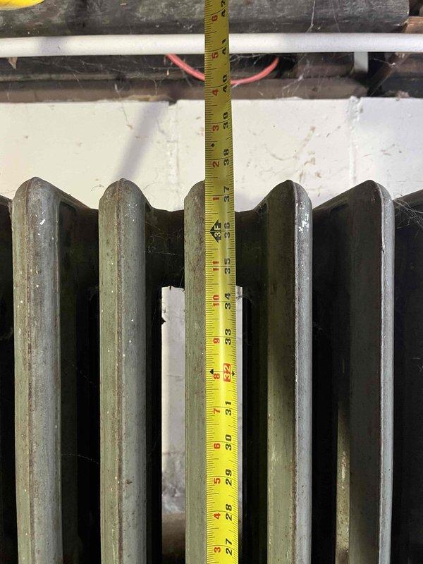 Conducted site assessment for boiler replacement lead from Sam K. Inspected existing heating system, which includes aged cast iron radiators showing signs of wear. Took detailed measurements of radiators to determine proper sizing for replacement equipment. Existing installation is mounted on cinderblock walls in basement utility area with visible aging infrastructure.