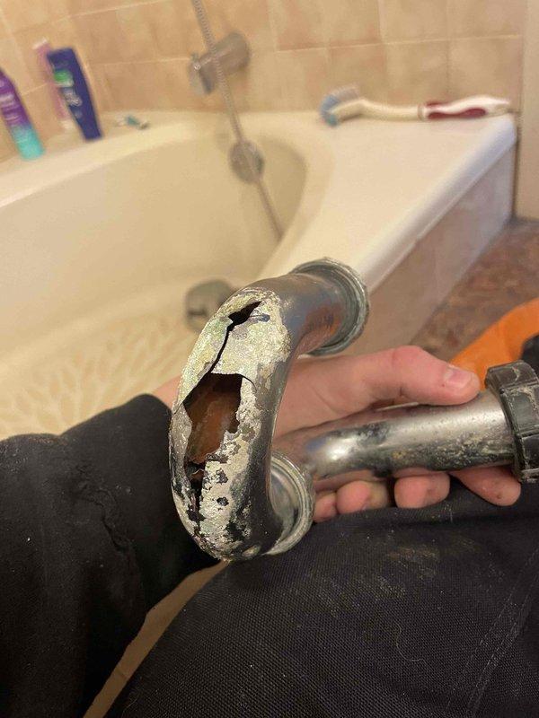 Responded to service call for bathroom sink leaking at the trap. Upon inspection, discovered severely damaged plumbing fixture with a large crack and significant corrosion. Removed and replaced the deteriorated p-trap assembly which showed extensive mineral buildup and calcification at connection points.