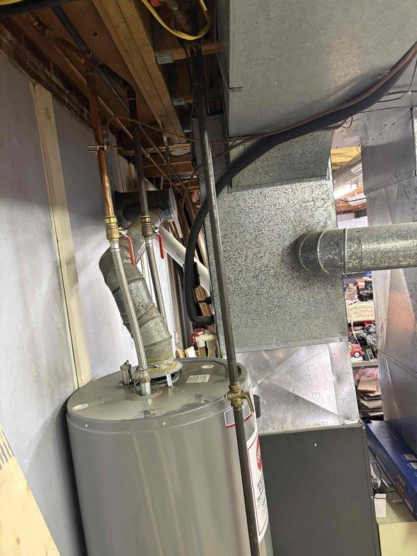 Inspected 17-year-old Goodman furnace system with connected AC unit in residential basement utility area. System is currently operational but showing age-related wear. Documented existing installation including ductwork configuration, water heater proximity, and PVC ventilation setup for potential replacement recommendation under senior discount program.