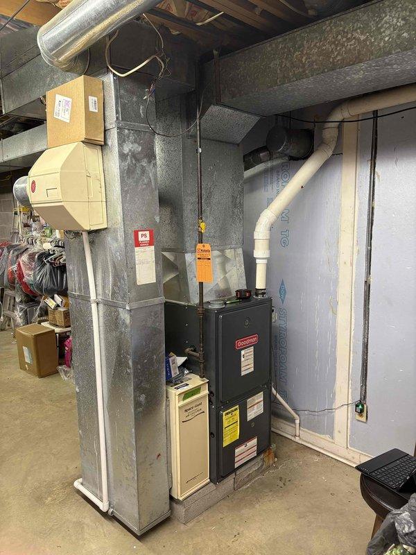 Inspected 17-year-old Goodman furnace system with connected AC unit in residential basement utility area. System is currently operational but showing age-related wear. Documented existing installation including ductwork configuration, water heater proximity, and PVC ventilation setup for potential replacement recommendation under senior discount program.