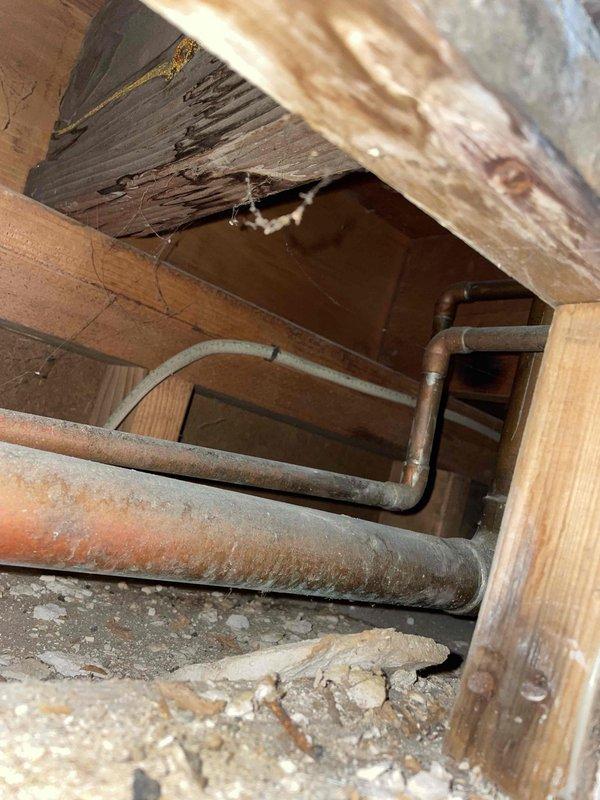 Inspected water leak from kitchen ceiling bulkhead. Upon investigation of the crawlspace, identified aged cast iron drain pipe with significant oxidation and deterioration. Observed moisture damage and discoloration on surrounding wooden joists and structural framing. Repaired compromised section of drain pipe and connections to PVC components to resolve the active leak.