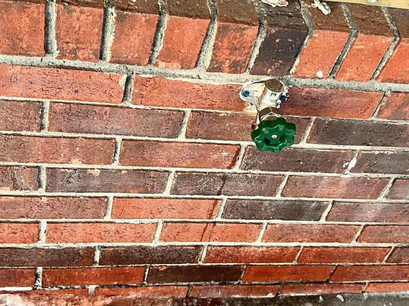 Responded to emergency service call for leaking exterior spigot that had worsened, requiring water shutdown to the property. Accessed interior wall plumbing through a drywall opening to reach the copper supply lines. Replaced the damaged wall-mounted brass spigot with new unit featuring green handle, restoring proper water service to the residence.