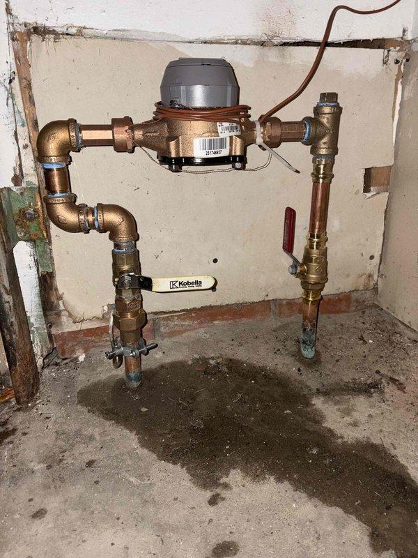 Responded to service call for frozen pipes and no heat. Inspected water meter installation and associated plumbing system showing signs of age and deterioration. Identified and addressed frozen pipe sections, ensuring proper water flow restoration. Confirmed functionality of the system with red shut-off valve and verified no active leaks in the copper and brass plumbing assembly.