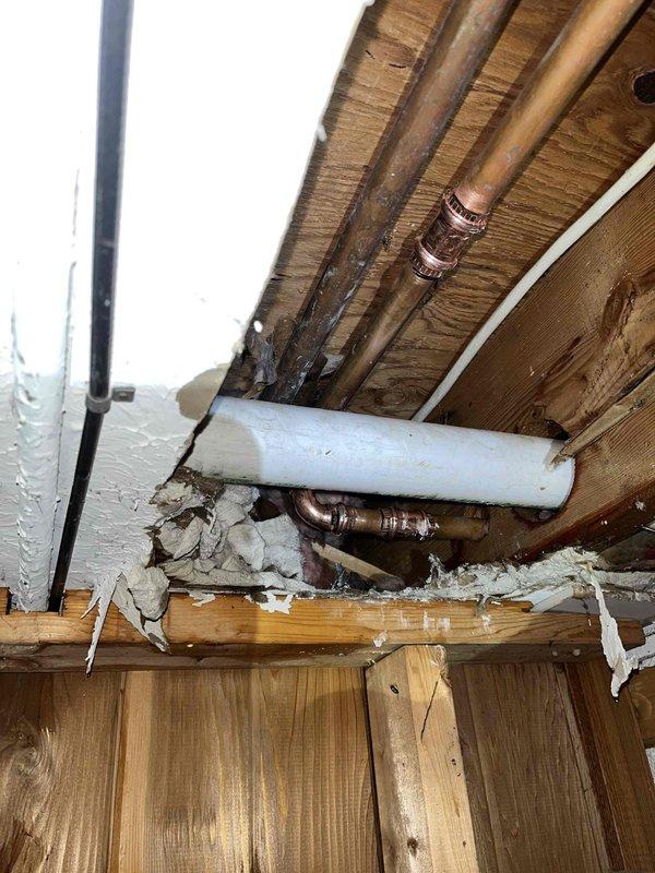 Responded to emergency call for burst pipe and no hot water. Upon inspection, discovered frozen pipes with one burst pipe causing water damage to interior structural components. Documented extensive damage to wooden joists and insulation. Identified multiple affected copper supply lines requiring repair to restore water service to the home.