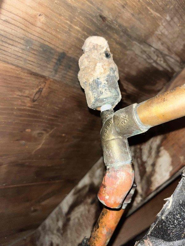Responded to service call for boiler-related leak in attic. Upon inspection, discovered a ruptured valve at the top of a pipe with significant mineral buildup and corrosion at connection points. Copper pipes showed varying degrees of oxidation with one pipe having degraded black insulation material. Repaired the burst valve to resolve the leak.