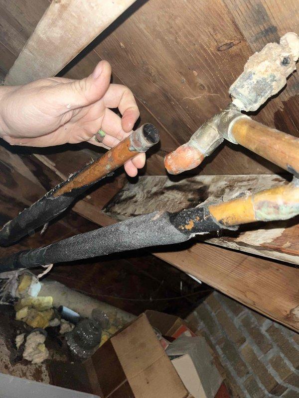 Responded to service call for boiler-related leak in attic. Upon inspection, discovered a ruptured valve at the top of a pipe with significant mineral buildup and corrosion at connection points. Copper pipes showed varying degrees of oxidation with one pipe having degraded black insulation material. Repaired the burst valve to resolve the leak.
