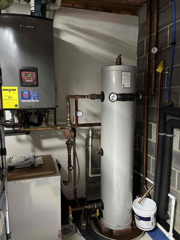 Inspected 50-gallon electric water heater that was showing minor leakage into the drain pan. Verified connections and pressure relief valve operation. Documented current condition with photos of the installation setup including adjacent Lochinvar heating unit and copper piping network. Recommended monitoring the leak and preparing for potential replacement if condition worsens.