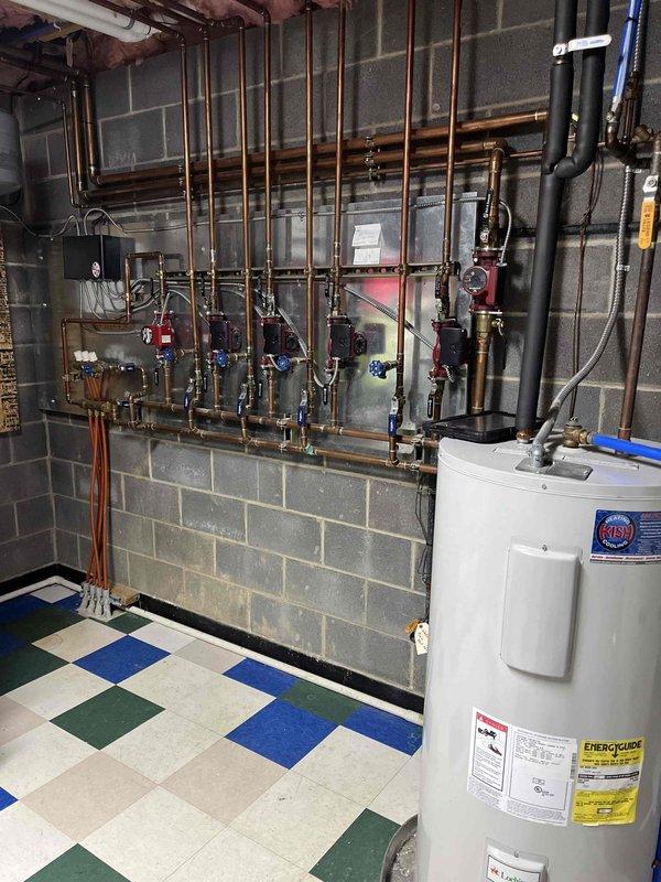 Inspected 50-gallon electric water heater that was showing minor leakage into the drain pan. Verified connections and pressure relief valve operation. Documented current condition with photos of the installation setup including adjacent Lochinvar heating unit and copper piping network. Recommended monitoring the leak and preparing for potential replacement if condition worsens.