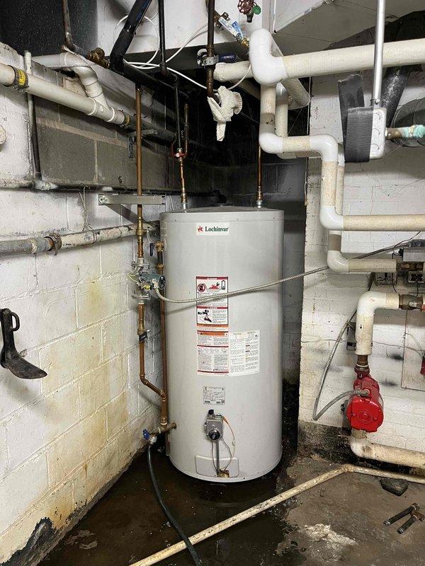 Responded to no hot water complaint. Inspected Lochinvar water heater system in utility room showing signs of moisture damage on surrounding concrete walls and floor. Noted unrelated damage to entry door frame with significant vertical cracking. Diagnosed and reset water heater, restoring hot water functionality.