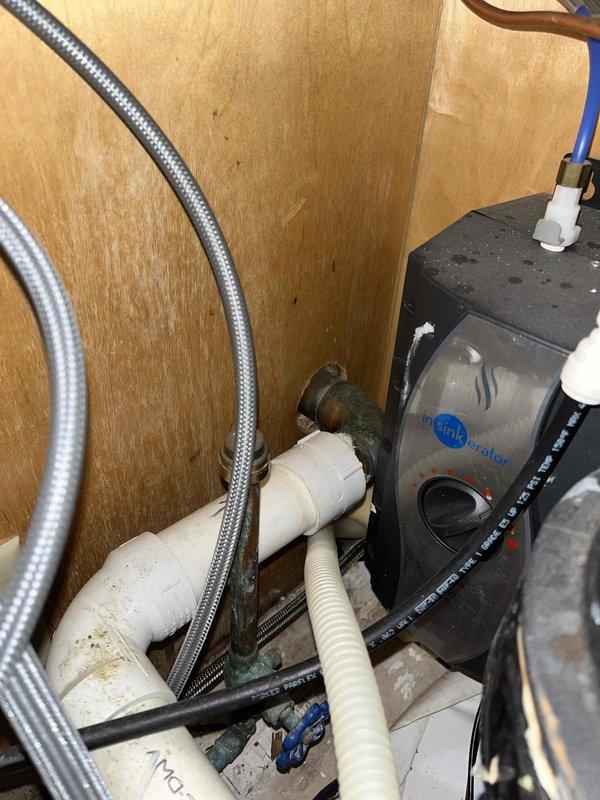 Responded to reported kitchen-to-basement water leak. Inspection revealed oxidation on copper pipe connection to InSinkerator disposal unit and water staining around pipe penetrations in cabinet. Serviced connection points and sealed pipe penetrations with foam insulation to prevent further leakage.