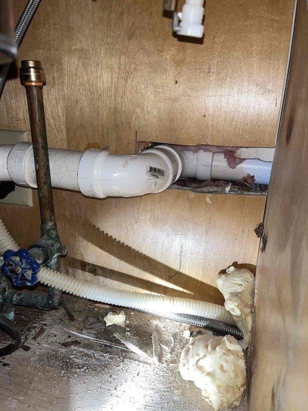 Responded to reported kitchen-to-basement water leak. Inspection revealed oxidation on copper pipe connection to InSinkerator disposal unit and water staining around pipe penetrations in cabinet. Serviced connection points and sealed pipe penetrations with foam insulation to prevent further leakage.