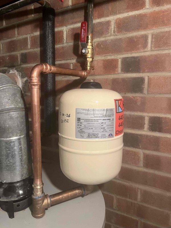 Inspected water heater system and diagnosed leaking expansion tank with visible corrosion trail on tank exterior. Removed damaged expansion tank and replaced with new 90 PSI expansion tank, properly connecting to existing copper piping system. Verified proper operation of new installation including pressure relief valve functionality.