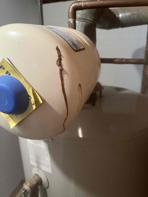 Inspected water heater system and diagnosed leaking expansion tank with visible corrosion trail on tank exterior. Removed damaged expansion tank and replaced with new 90 PSI expansion tank, properly connecting to existing copper piping system. Verified proper operation of new installation including pressure relief valve functionality.