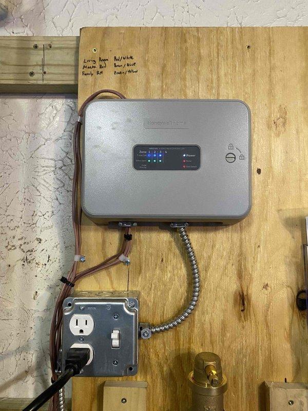 Completed boiler installation with Honeywell zone control system mounted on wooden panel, properly labeled for different rooms including Living Room and Family Room. Ensured proper leveling of PVC piping in the attic space and verified insulation integrity around installation area. Temporary space heaters were returned as requested.