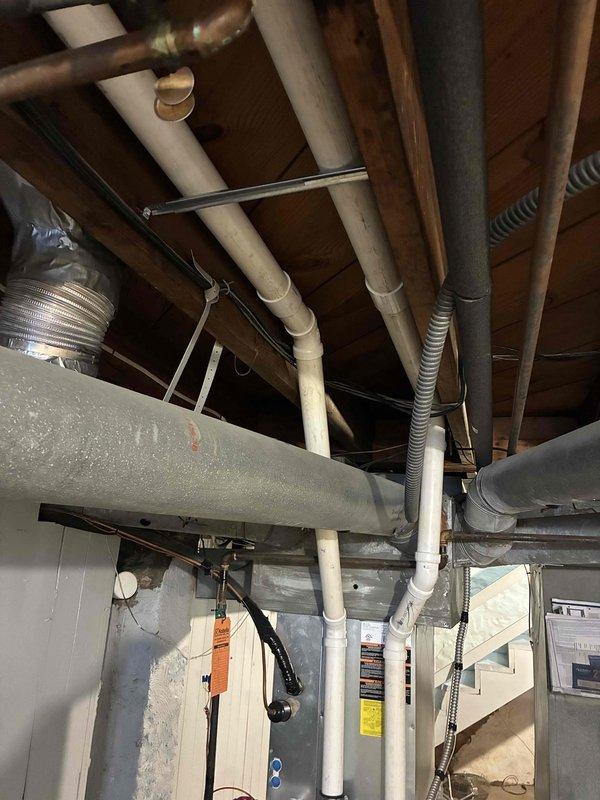 Completed installation of ductwork in basement utility area, routing insulated metal ducts through floor joists and connecting to existing HVAC system. Installed proper pipe penetrations through wooden structural members with fiberglass insulation for thermal efficiency. Coordinated with JondzEvan regarding chimney venting components to complete the installation.