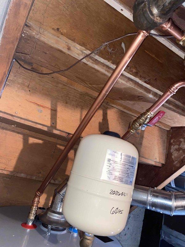Completed installation of a tanked water heater with associated copper pipe connections and expansion tank (labeled 602022/602). Installation included proper mounting of the expansion tank, connection to existing plumbing system, and installation of control valves including red-handled and blue-handled shutoffs. All connections were verified secure with no leaks observed.