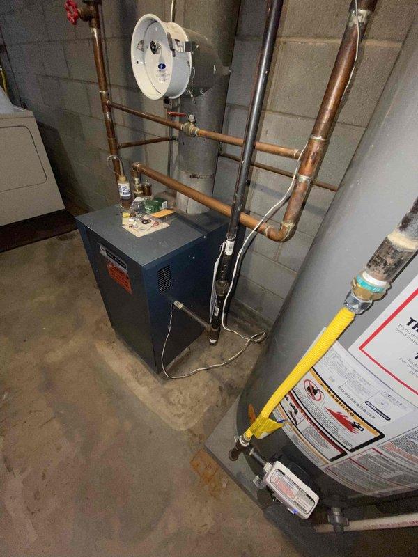 Conducted boiler system evaluation for a two-story home with heating imbalance issues - upstairs cold while first floor maintains adequate heating. Inspected existing hydronic heating system in basement mechanical room, including blue boiler unit, copper piping network, and associated controls. Documented current thermostat configuration and temperature differentials between floors to determine appropriate solution for balanced heating distribution.
