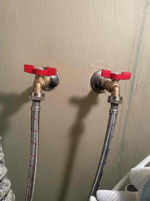 Replaced two deteriorating washer shut-off valves with new brass quarter-turn valves featuring red handles. Installed stainless steel braided supply lines for improved durability and leak prevention, ensuring proper water supply connection to the washing machine.