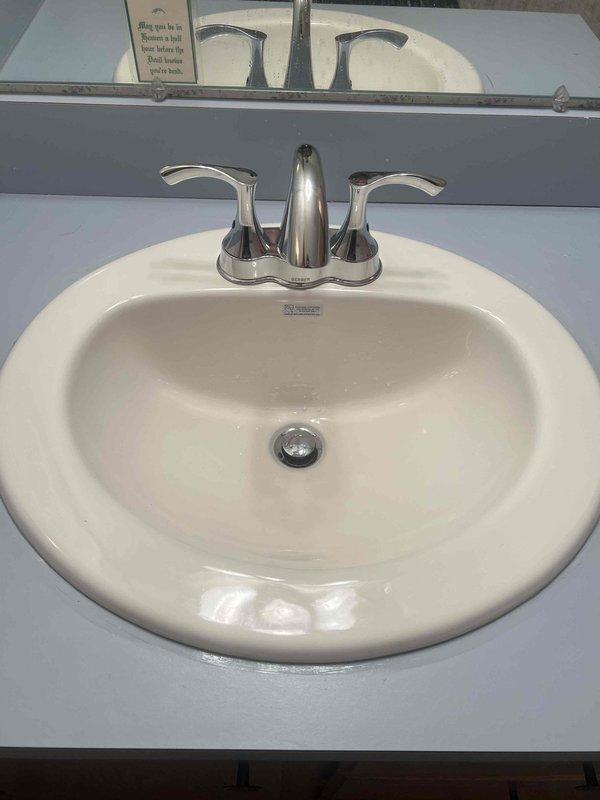 Completed removal of existing bathroom sink and installed new customer-purchased oval white porcelain sink with chrome dual-handle faucet in light blue/gray countertop. Connected new braided stainless steel supply lines to existing copper water lines and installed new PVC p-trap drain assembly. Work order fulfilled as sold, with all materials previously ordered and now successfully installed.