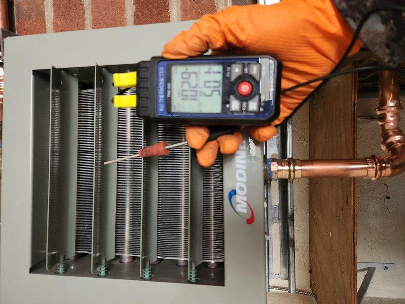 Completed installation of Modine boiler system, performing post-installation diagnostics with temperature readings (62.0°F/59.9°F) at the heat exchanger. Verified proper leveling of the unit using spirit level and confirmed all connections were properly secured against the brick wall mounting location.
