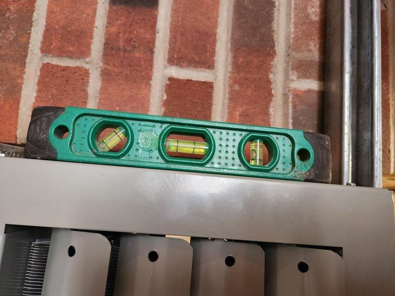 Completed installation of Modine boiler system, performing post-installation diagnostics with temperature readings (62.0°F/59.9°F) at the heat exchanger. Verified proper leveling of the unit using spirit level and confirmed all connections were properly secured against the brick wall mounting location.