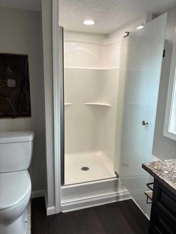 Completed inspection of bathroom plumbing renovation featuring new shower installation with acrylic surround and glass door. Evaluated basement utility space PVC piping configuration with multiple 90-degree joints and connections for drainage/water supply system. All pipe joints properly sealed with appropriate adhesive as indicated by purple markings.