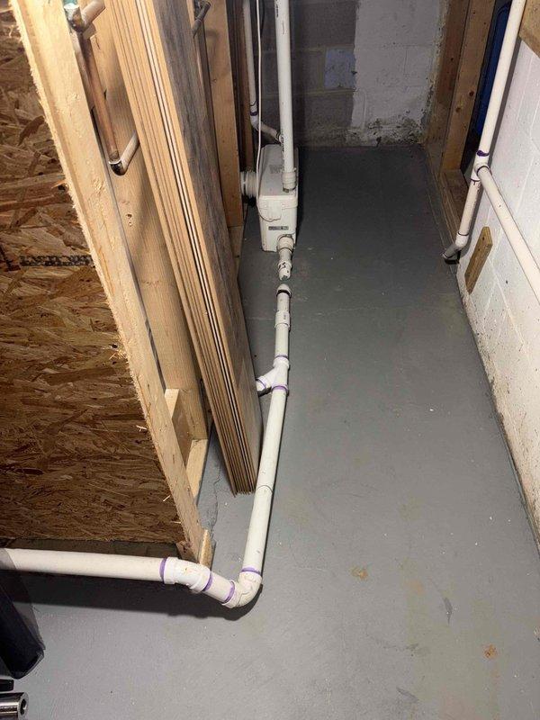 Completed inspection of bathroom plumbing renovation featuring new shower installation with acrylic surround and glass door. Evaluated basement utility space PVC piping configuration with multiple 90-degree joints and connections for drainage/water supply system. All pipe joints properly sealed with appropriate adhesive as indicated by purple markings.