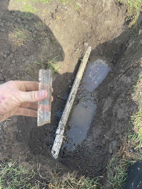 Located and excavated buried sump pump discharge pipe using electronic utility detector (512Hz frequency). Upon inspection, discovered clogged discharge line with standing water pooling at excavation site; cleared blockage to restore proper pump function.