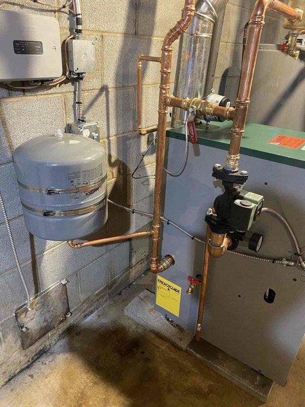 Completed boiler installation as previously sold. Installation included mounting water heater with appropriate labeling, connecting copper and PVC piping with shutoff valves, installing expansion tank with proper wall mounting, and setting up circulation pump with green housing. System features complete with pressure gauges and vent piping, all professionally installed in basement utility area.