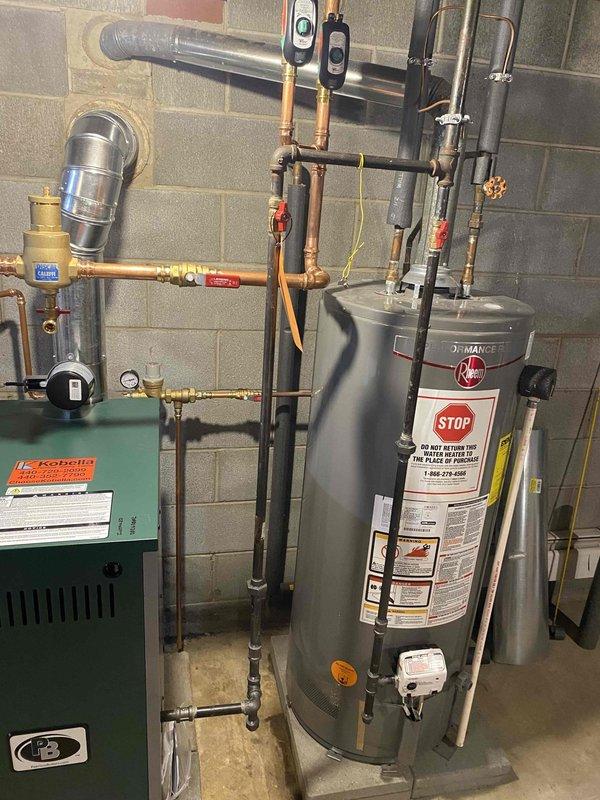 Completed boiler installation as previously sold. Installation included mounting water heater with appropriate labeling, connecting copper and PVC piping with shutoff valves, installing expansion tank with proper wall mounting, and setting up circulation pump with green housing. System features complete with pressure gauges and vent piping, all professionally installed in basement utility area.
