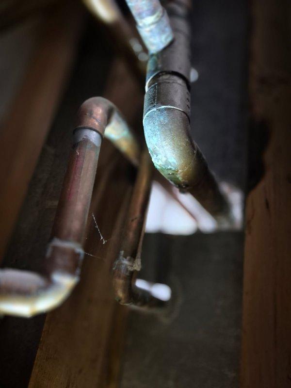 Repaired leaking copper pipe joint on hot water line connected to boiler system. Identified significant green-blue corrosion at connection point, indicating prolonged moisture exposure. Replaced damaged fitting and verified system integrity with pressure test.