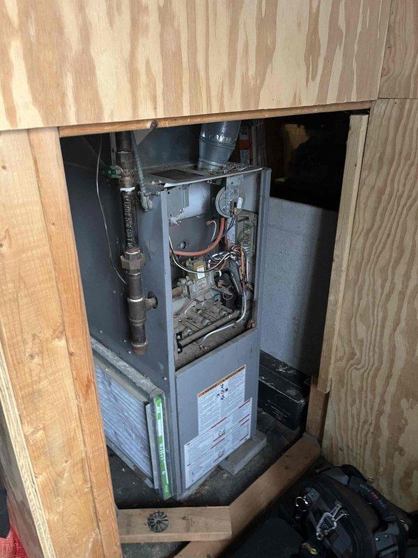 Performed diagnostic service on aging furnace with reported loud exhaust fan. Inspection of the unit, installed in wooden compartment, revealed worn blower motor assembly and pressure switch mechanism requiring attention. Service included cleaning components, lubricating motor bearings, and adjusting pressure switch connections to resolve noise issue and restore proper heating function.