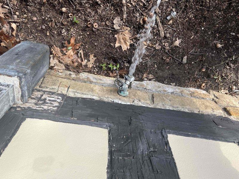 Responded to service call for an actively leaking outdoor spigot mounted on stone/concrete ledge. Identified deterioration at exterior foundation corner where galvanized pipe connects to building. Repaired leak by replacing damaged valve connection and applied waterproof sealant in L-shaped pattern across concrete surface to prevent further water intrusion.