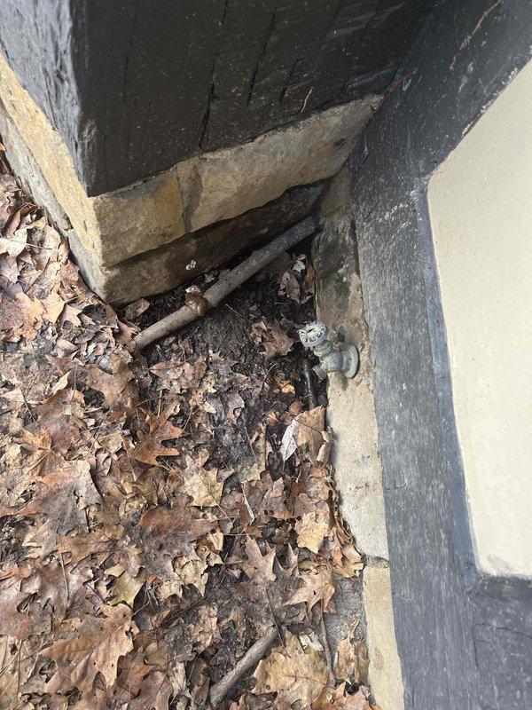 Responded to service call for an actively leaking outdoor spigot mounted on stone/concrete ledge. Identified deterioration at exterior foundation corner where galvanized pipe connects to building. Repaired leak by replacing damaged valve connection and applied waterproof sealant in L-shaped pattern across concrete surface to prevent further water intrusion.