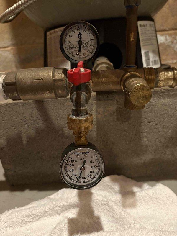 Diagnosed low water pressure issue by inspecting pressure gauges in the main supply line showing readings below normal parameters. Identified clogged filtration system as the source of restriction; performed maintenance on the blue circular filter assembly including a complete flush cycle to remove sediment buildup. Restored system pressure to optimal levels as verified by post-service gauge readings.