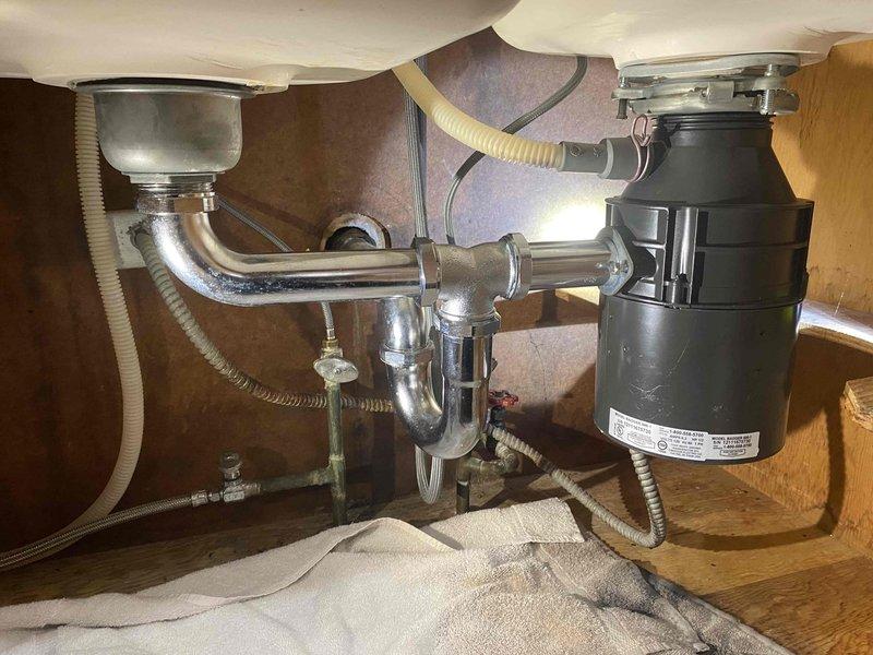 Responded to a water leak complaint where customer suspected the garbage disposal as the source. Upon inspection of the under-sink plumbing system, evaluated the black garbage disposal unit connected to chrome P-trap assembly and associated drain lines. Removed the garbage disposal as requested to eliminate the suspected leak source.
