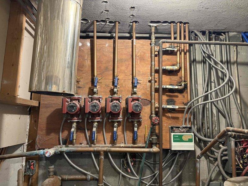Conducted on-site assessment for replacement of outdated coal burner with new gas boiler system to power existing radiant floor heating. Evaluated current hydronic distribution system featuring four zone circulation pumps mounted on wooden backboard with associated copper piping, valves, and pressure gauges. Inspected connection points for proper integration with existing PVC piping and identified optimal location for new boiler installation while documenting current mechanical connections and electrical requirements.