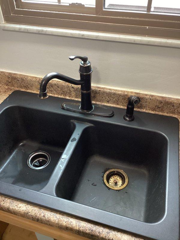 Completed service on two-basin black kitchen sink with leaking faucet. Diagnosed issue with main faucet assembly and performed necessary repairs to resolve the leak. Additional inspection revealed mineral buildup in drain strainer which was cleaned to ensure proper drainage.