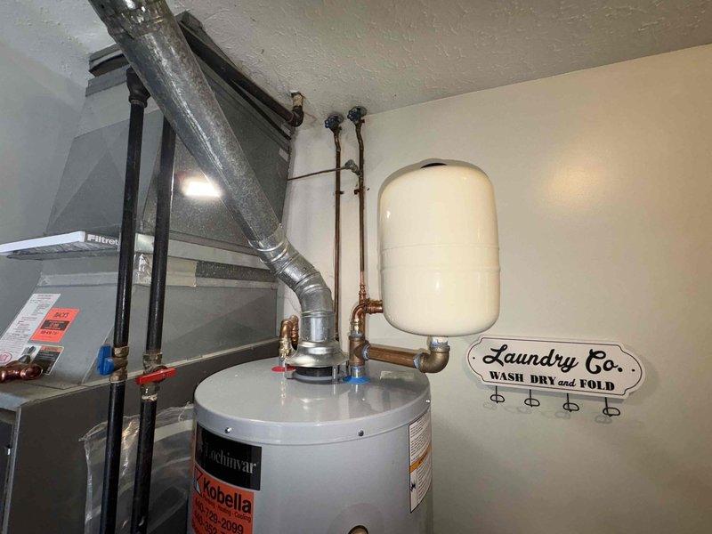 Responded to service call for Lochinvar water heater with active tank leak. Inspection confirmed slow drip from bottom of tank indicating tank failure. Documented condition with photos showing complete installation including expansion tank, copper piping, and venting configuration for replacement recommendation.