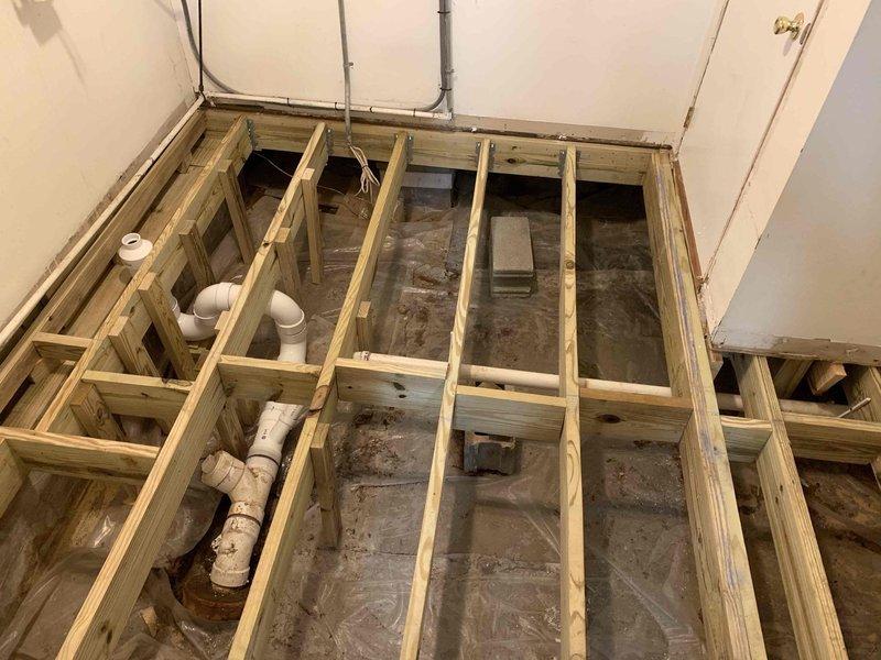 Completed excavation work to relocate sewer line for new toilet installation in utility room, exposing existing PVC drainage pipe alongside house foundation. Prepared subfloor with wooden framing structure and installed necessary plumbing connections to accommodate replacement of instant electric water heater with instant gas water heater using existing gas line.