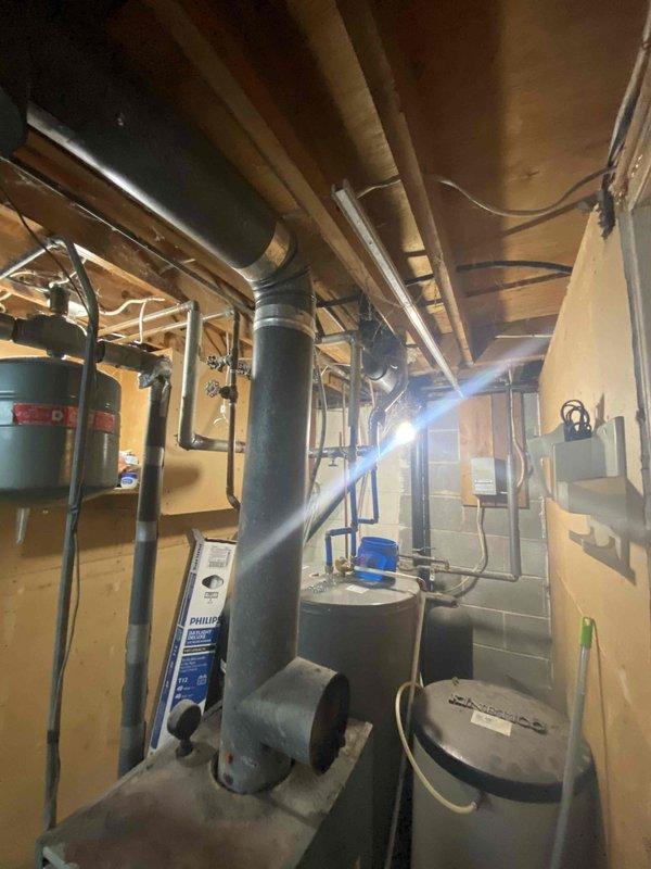 Conducted site assessment of current oil boiler system located in basement utility area. Evaluated existing equipment including ductwork, exhaust piping, and adjacent water heater to determine feasibility of fuel conversion options as requested by customer. Photos documented current installation configuration for reference in preparing comprehensive fuel-type change proposal.