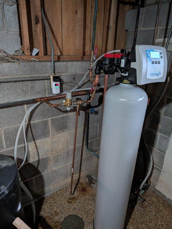 During club maintenance visit, identified corrosion on several fittings and a leaking pressure relief pipe on boiler system installed in 2024. Documented issues with photographs showing oxidation on copper piping and possible water damage to surrounding area as evidenced by discoloration in the gravel bed beneath plumbing connections.