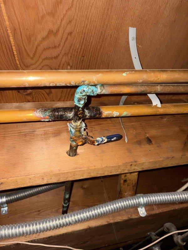 Addressed leaking copper water line in basement of 60-year-old home. Discovered significant corrosion and oxidation at pipe junction with blue-green patina (verdigris) on multiple connection points. Replaced deteriorated section and valve assembly to resolve ongoing moisture issue.