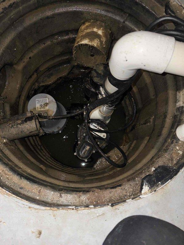 Responded to service call for sump pump alarm activation that had been occurring for approximately two weeks. Upon inspection, found the sump basin containing standing water with the pump submerged and operational. Examined exterior discharge pipe configuration and confirmed proper installation with no visible damage or blockage. Verified system functionality and addressed alarm issue.