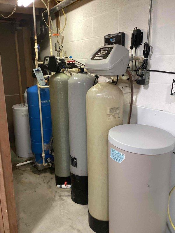 Responded to emergency service call for complete loss of water supply in 30-year-old residence. Inspected comprehensive water treatment system in basement consisting of multiple filtration tanks (blue, gray, and beige) and Wellxtrol pressure tank. Diagnosed pressure tank failure, replaced defective component, and restored water service to entire house.