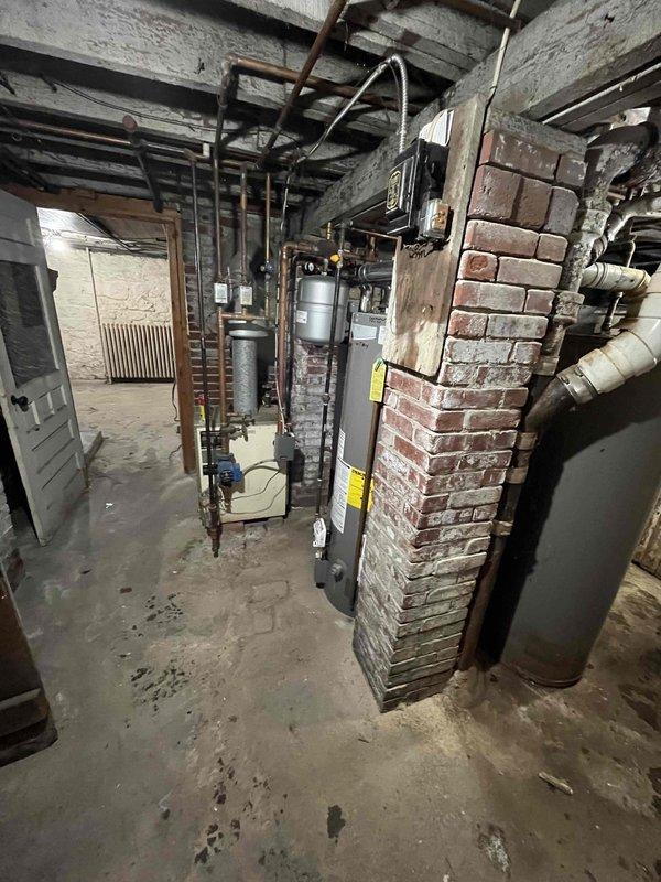 Inspected cast iron drain line serving upper apartment that exhibited active leakage in basement area. Documented existing conditions including visible water damage on concrete floor and aging plumbing infrastructure connected to water heating system. Determined job requires comprehensive repair beyond initial assessment; scheduled follow-up visit to complete necessary drainage system repairs.